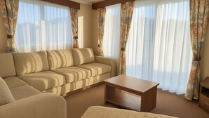 A living room with a beige sofa, a wooden coffee table, and a patterned curtain. - Freshwater Beach Holiday Park - Holiday Accommodation 12281 (Bridport)