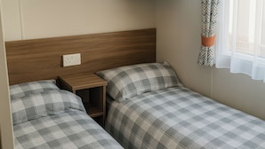A bedroom with two beds, wooden headboard, bedside tables, and a window with curtains. - Freshwater Beach Holiday Park - Holiday Accommodation 12281 (Bridport)