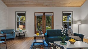 Un salón moderno con un sofá azul, una mesa de centro con un cuenco de limones, una alfombra estampada y vistas a un jardín a través de grandes ventanales.