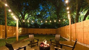 Un área de patio al aire libre con un brasero, sillas de madera y luces colgantes.