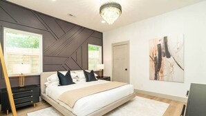 Un dormitorio moderno con una cama grande, paredes de acento oscuras y una araña.