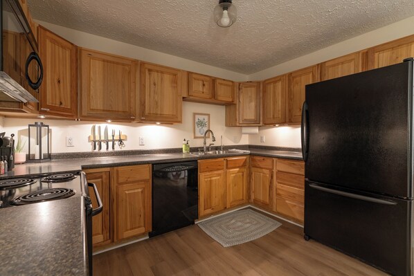 Una cocina con armarios de madera, un refrigerador negro, una estufa y un lavavajillas.