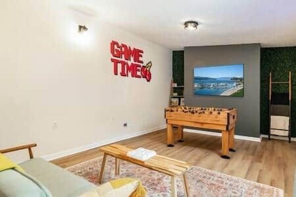 A living room with a foosball table, a sofa, and a wall-mounted TV.