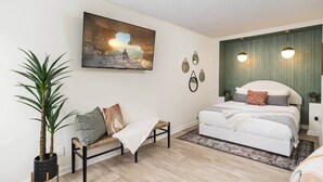 Un dormitorio moderno con una cama, un banco, una planta en maceta y un cuadro en la pared.