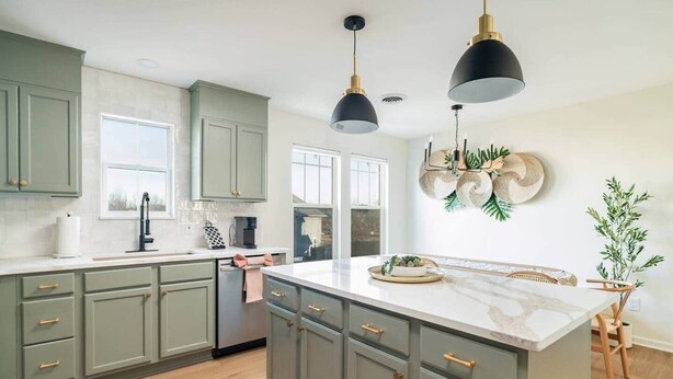 A kitchen with light green cabinets, a marble island, pendant lights, and a potted plant.
