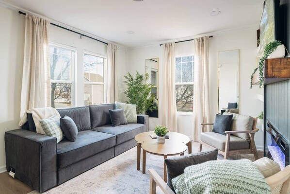Un salon comprenant un canapé, un fauteuil, une table basse et une grande fenêtre avec des rideaux.