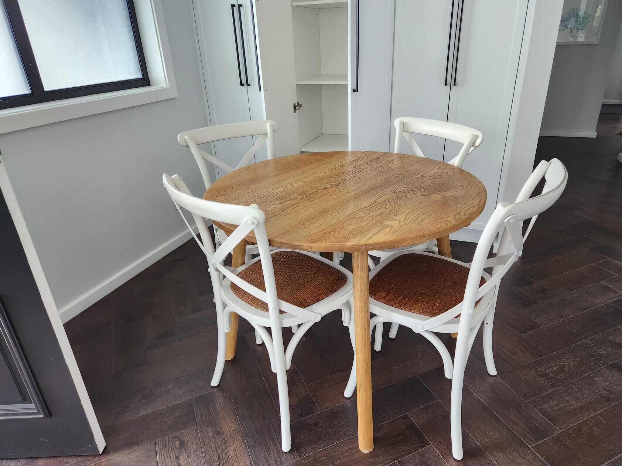A round wooden dining table with white chairs, set in a room with dark wooden flooring and white walls.