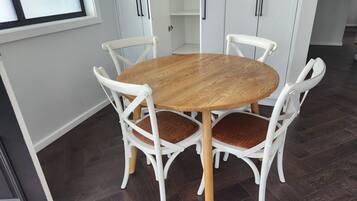 A round wooden dining table with white chairs, set in a room with dark wooden flooring and white walls.