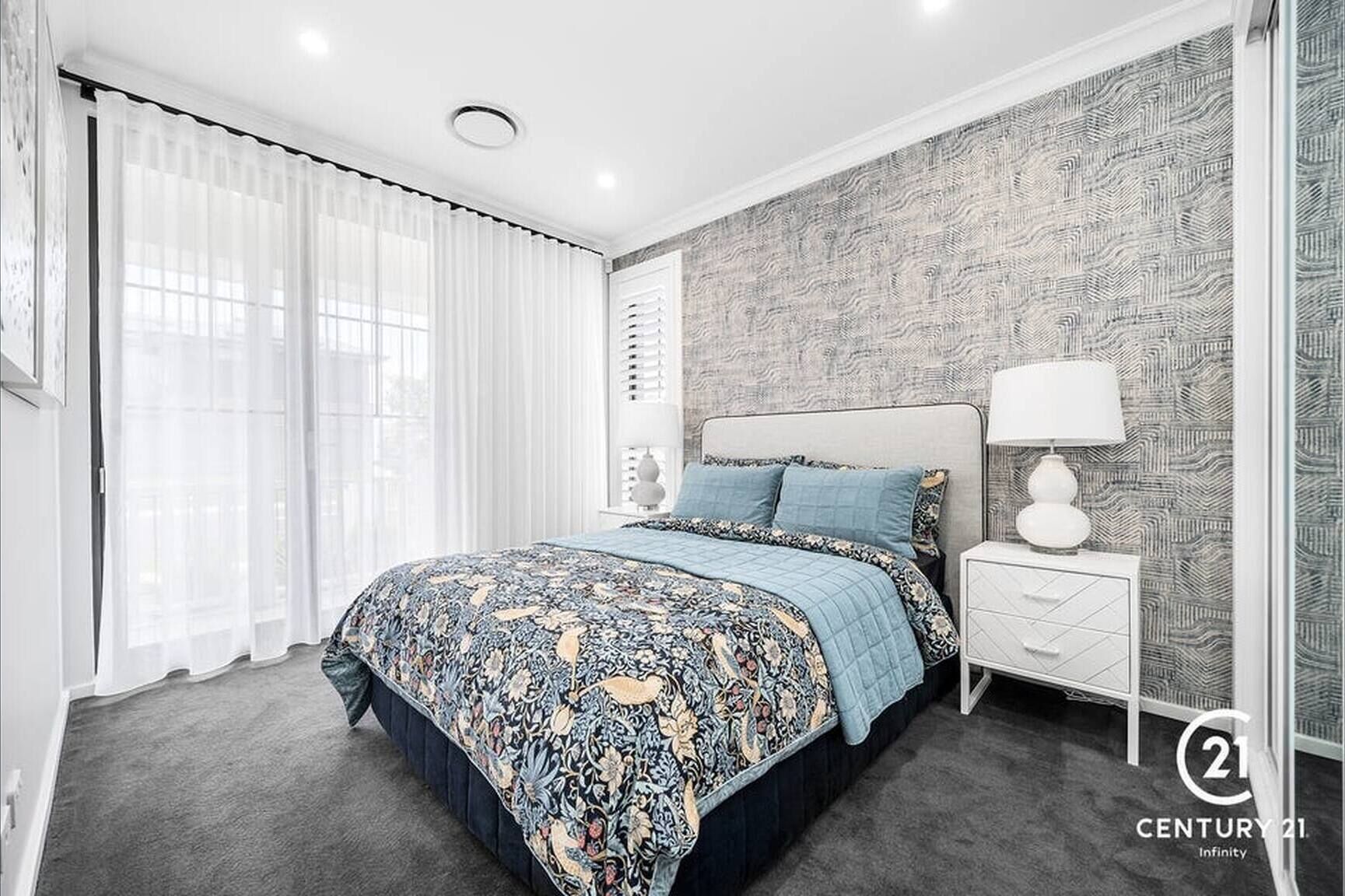 A modern bedroom with a patterned bedspread, a nightstand with a lamp, and a patterned wallpaper.