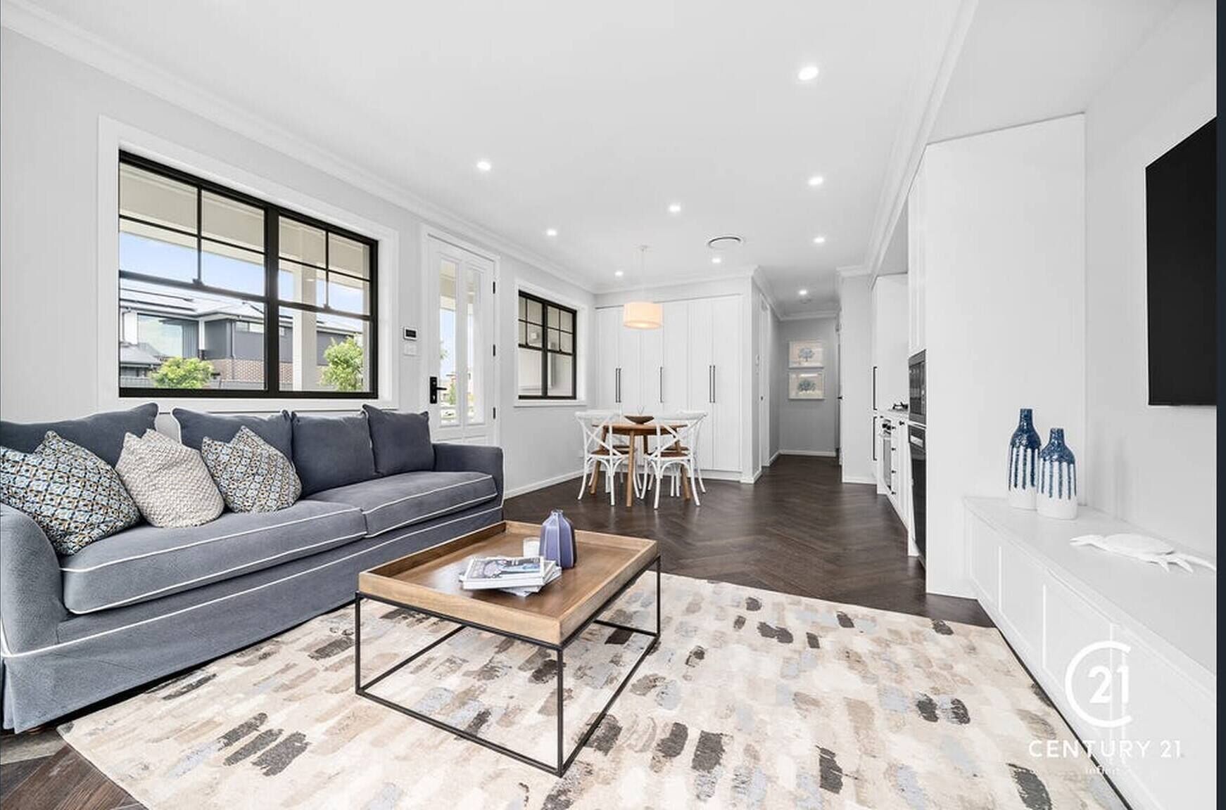 A modern living room with a grey sofa, a coffee table, and a dining area with white chairs.