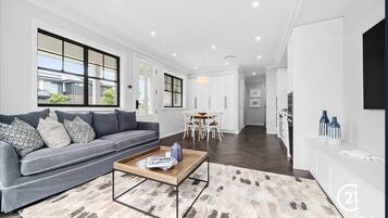 A modern living room with a grey sofa, a coffee table, and a dining area with white chairs.
