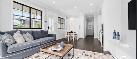 A modern living room with a grey sofa, a coffee table, and a dining area with white chairs.