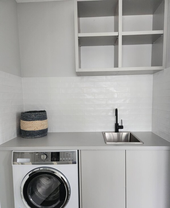 Un espace buanderie compact comprenant un lave-linge, un évier et un meuble de rangement.