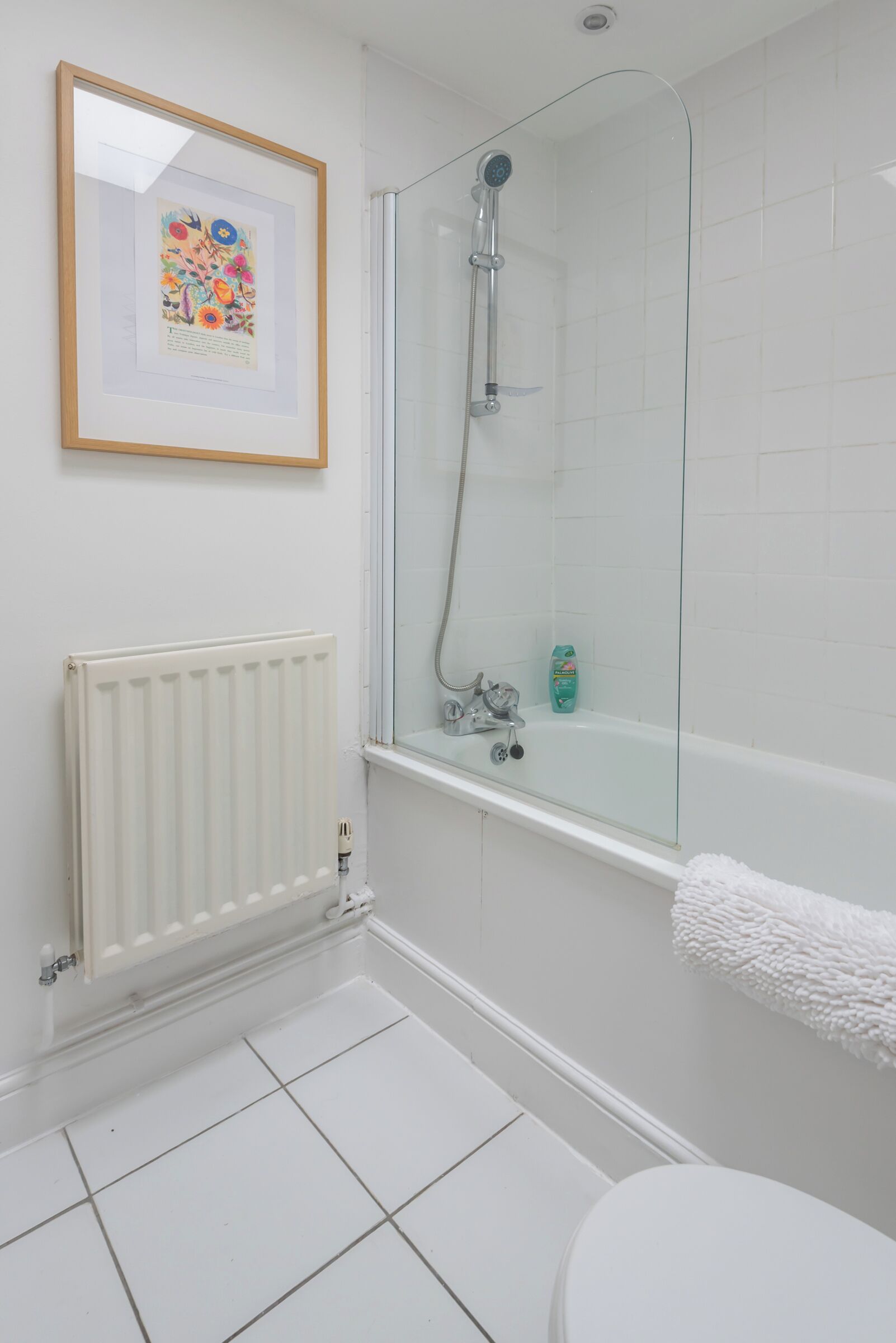 A bathroom with a glass-enclosed shower, a white radiator, and a framed artwork on the wall.