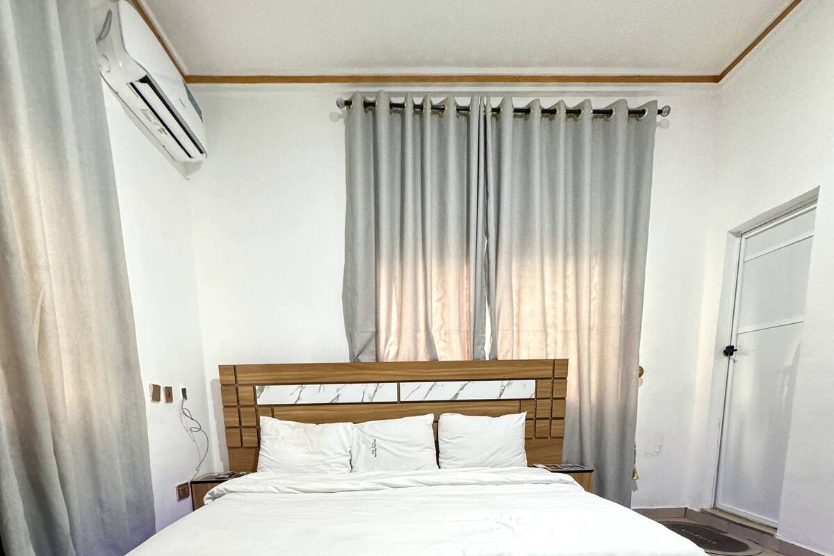 A bedroom with a bed, curtains, an air conditioning unit, and a door.