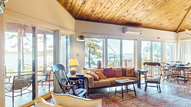 A spacious living area with a wooden ceiling, large windows, and a view of the outdoors.