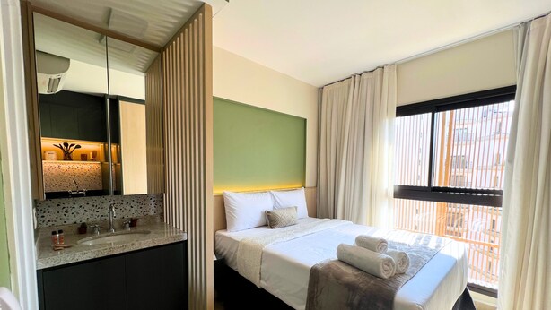 A hotel room with a bed, a bathroom, and a window with curtains. - Ibirapuera Park (São Paulo)