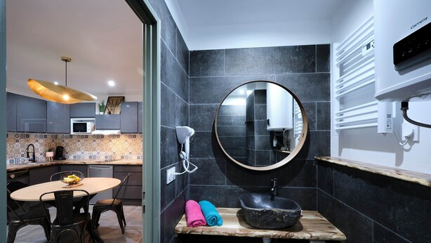 A modern bathroom with a round mirror, black sink, and a wooden vanity. - Confort & Calme - Air-conditioned T2 with central courtyard (Carcassonne)