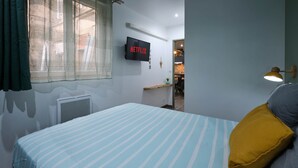 A bedroom with a bed, a TV mounted on the wall, and a window with curtains. - Confort & Calme - Air-conditioned T2 with central courtyard (Carcassonne)