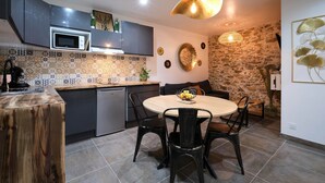 A modern kitchen with a round dining table, black chairs, a microwave, and a stone wall. - Confort & Calme - Air-conditioned T2 with central courtyard (Carcassonne)
