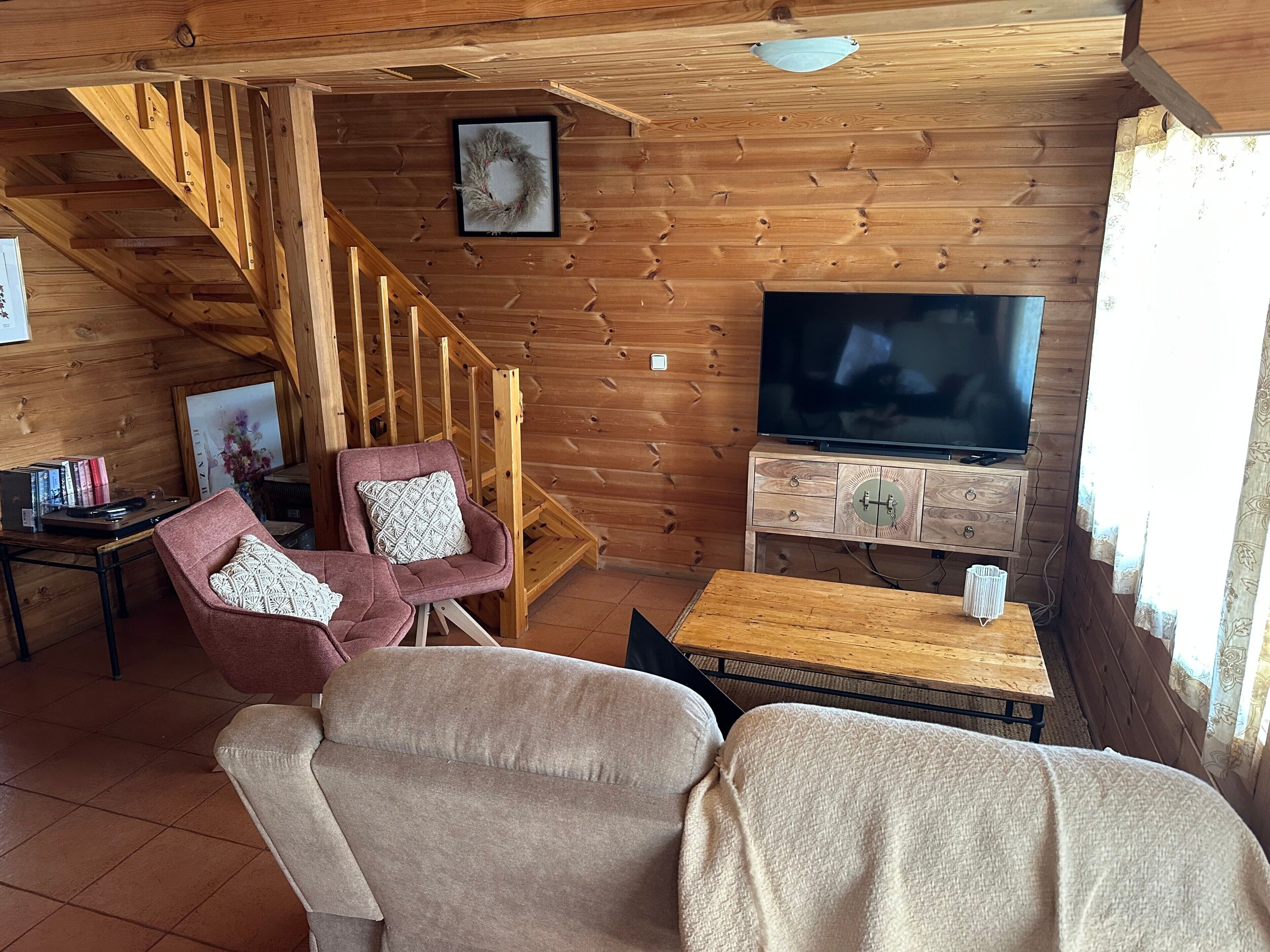 Un intérieur en bois comprenant un téléviseur, deux fauteuils, une petite table et un escalier.