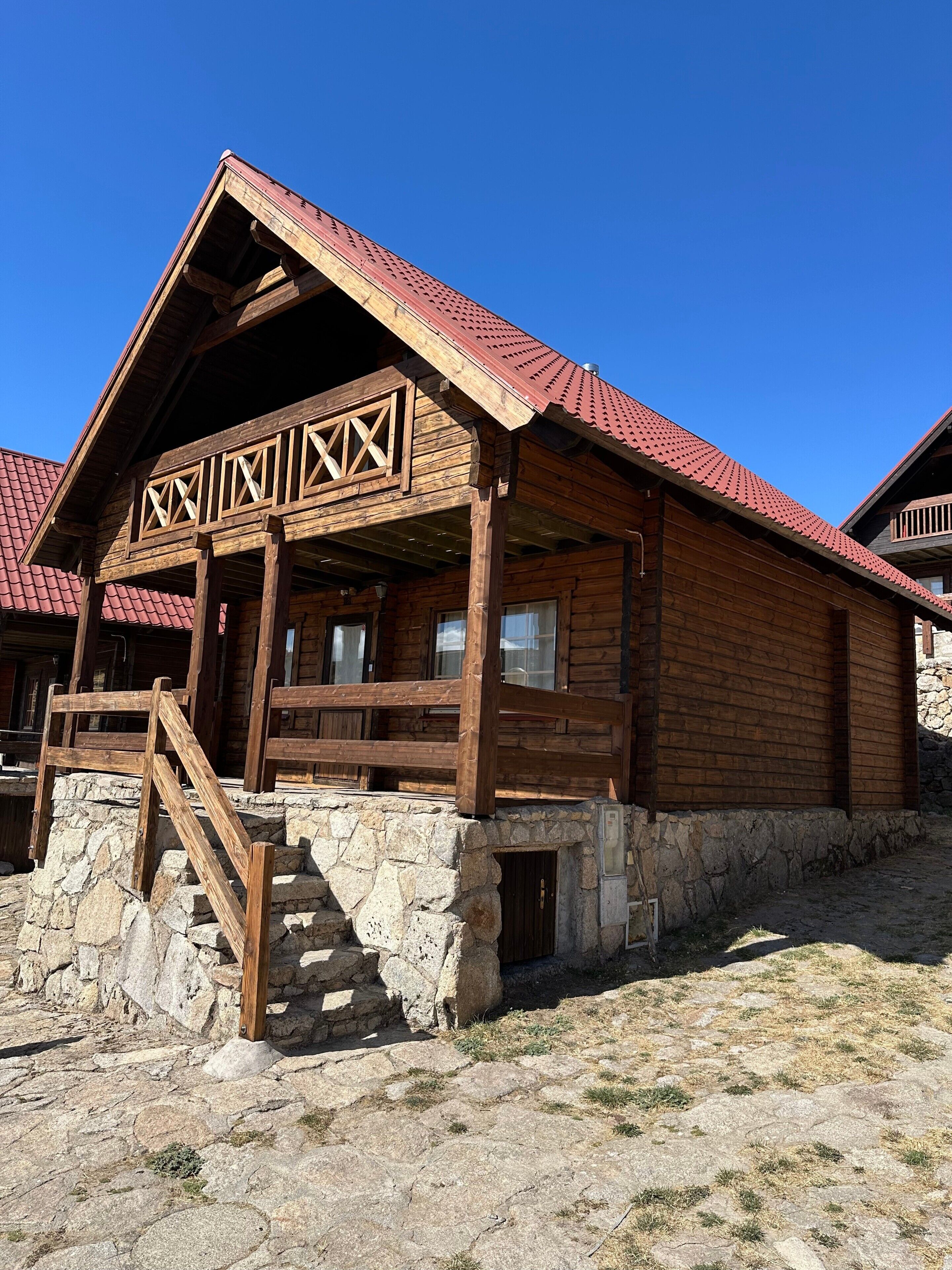 Une cabane en bois avec des fondations en pierre, une véranda en bois et un toit rouge.