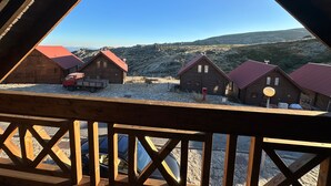 Eine Holzhütte mit rotem Dach, ein Kleinlastwagen und ein freier Blick auf eine gebirgige Landschaft.