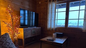 Ein gemütliches Cabin-Interieur mit Fernseher, Holzmöbeln, einem Fenster mit Aussicht und einer Zierpflanze.