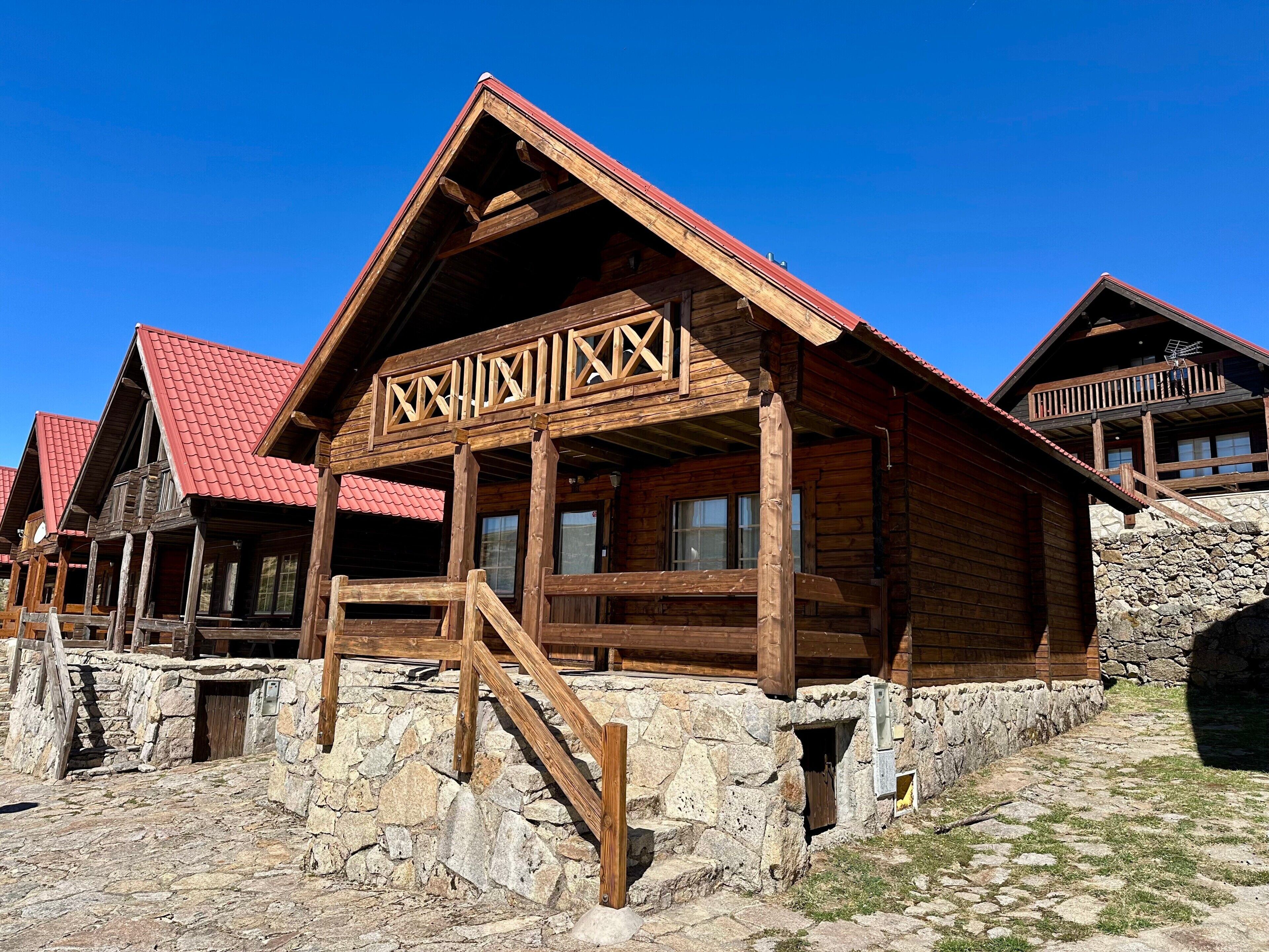 Une cabane en bois avec des fondations en pierre, un balcon en bois et un toit rouge.