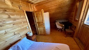 Ein Zimmer einer Holzhütte mit einem Bett, einem kleinen Tisch und einem Stuhl.