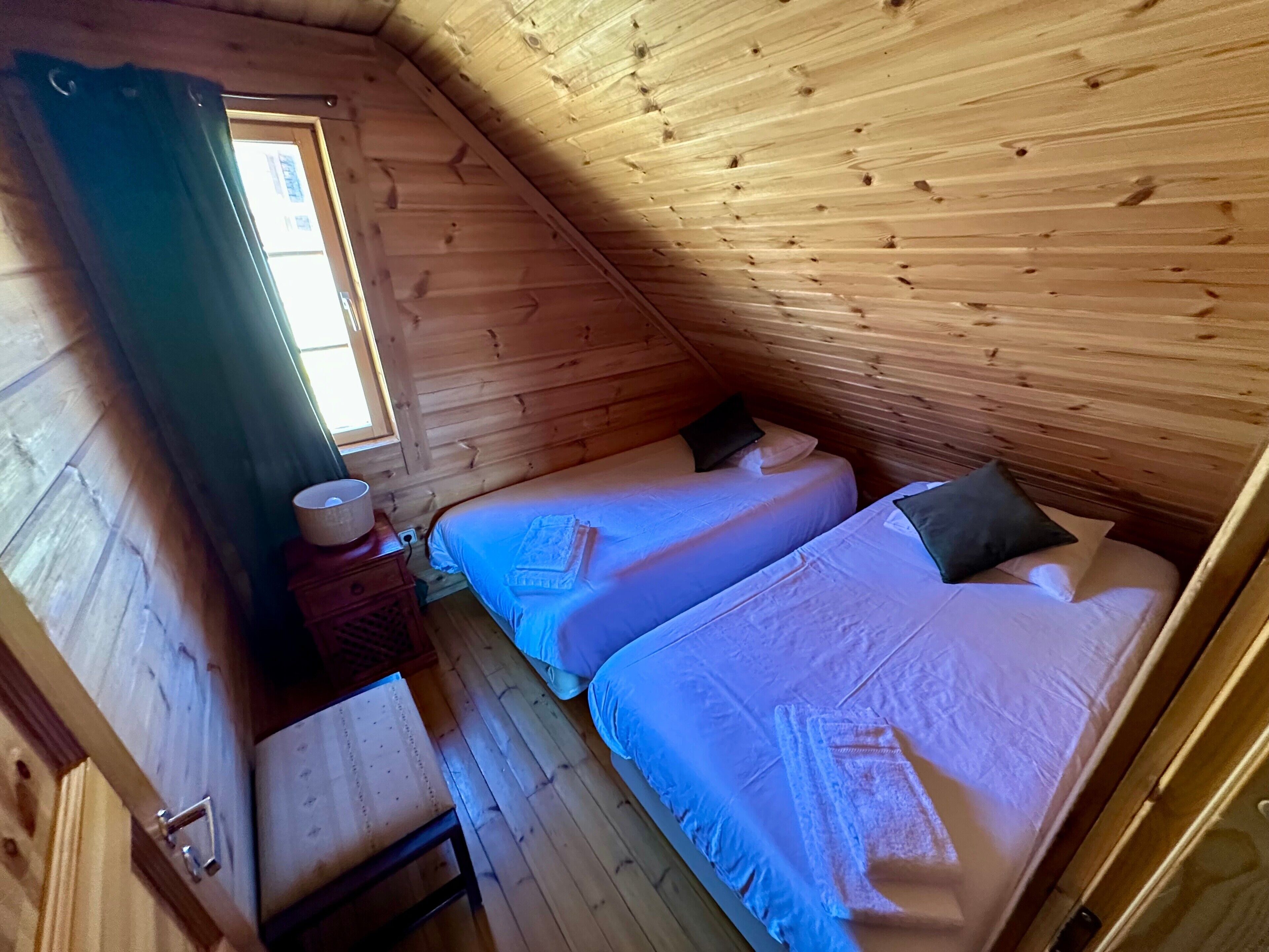 A wooden cabin room with two beds, a small table, and a window.