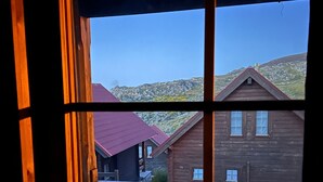 Eine Holzhütte mit rotem Dach, einer Holzdiele und Blick auf eine gebirgige Landschaft.