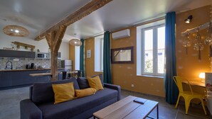 Una sala moderna con un sofá, una mesa de madera y una silla amarilla. Hay una zona de cocina con un microondas y un lavamanos.