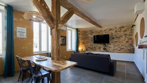 Una sala de estar acogedora con una pared de piedra, un televisor de pantalla plana, una mesa de comedor de madera con sillas y un sofá oscuro.