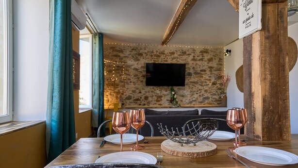 Un comedor con una mesa de madera dispuesta para dos personas, dos copas de vino y un centro de mesa decorativo de metal.