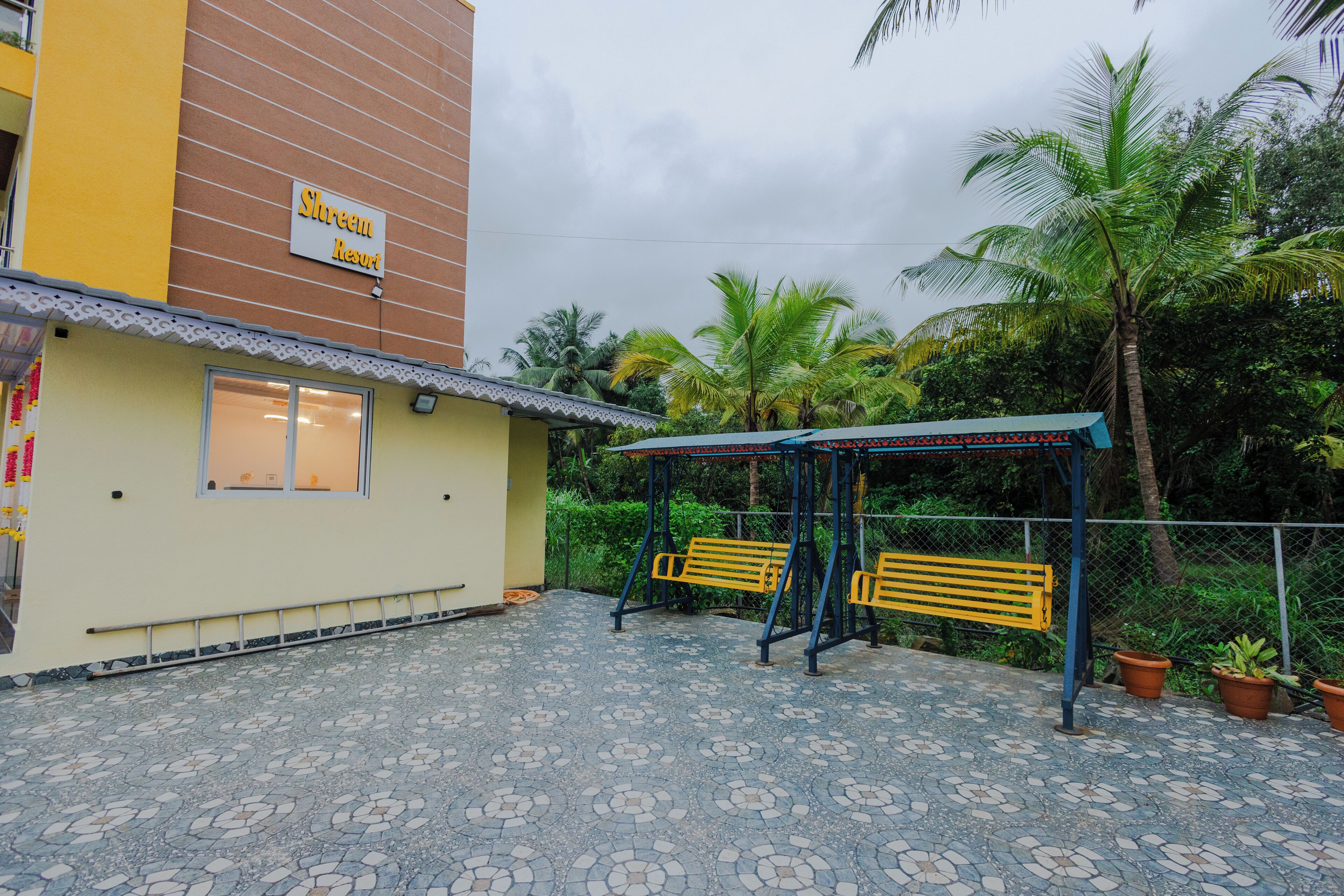 A building with a sign reading "Shreem Resort," a covered seating area with benches, and a tiled patio.