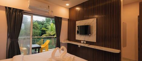 A hotel room with a bed, a TV mounted on the wall, a balcony with a view of greenery, and an air conditioning unit.
