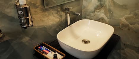 Un baño con un lavamanos blanco, un dispensador de jabón y una pequeña bandeja con artículos de aseo.