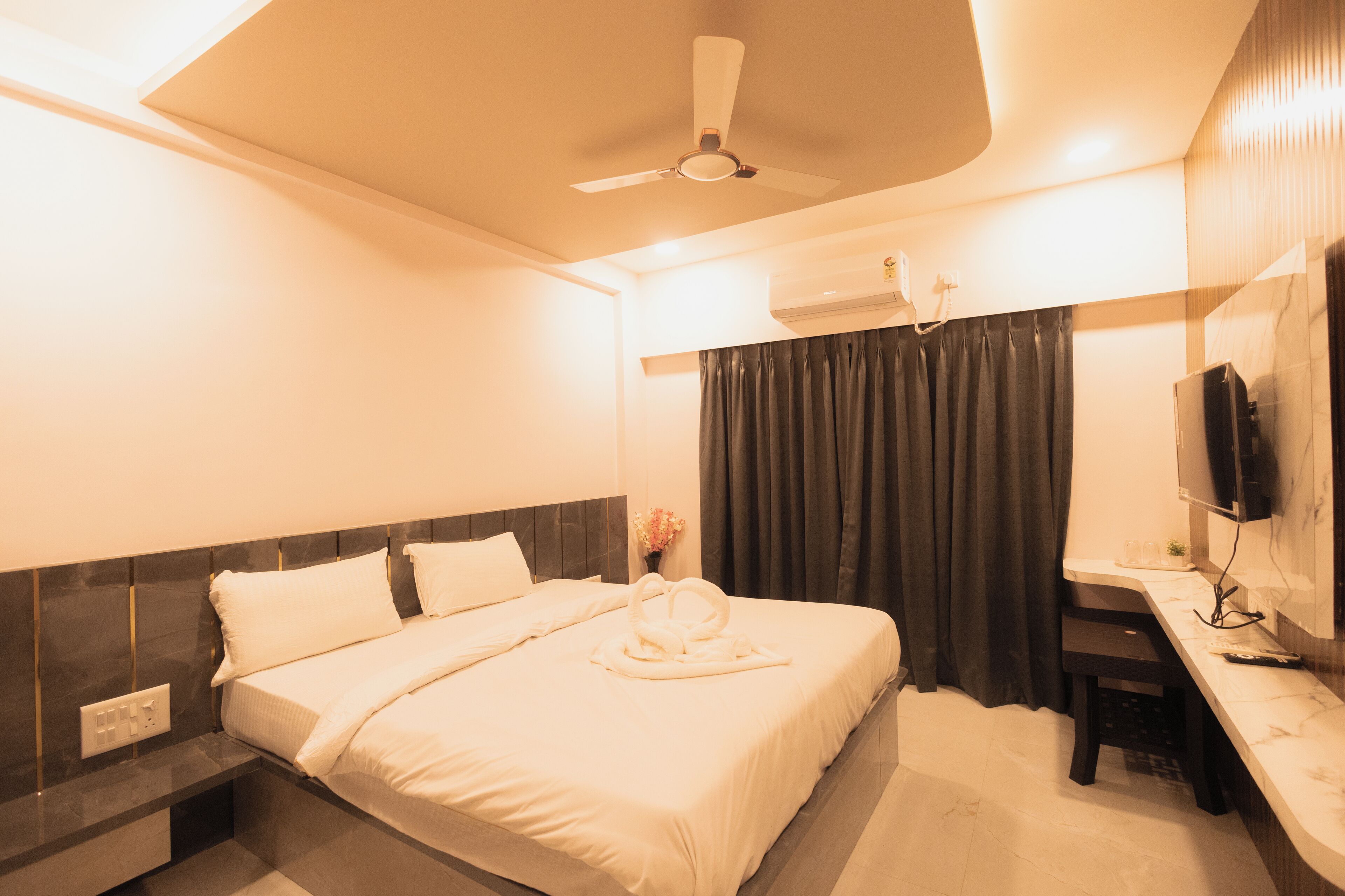 A hotel room with a bed, bedside table, TV, and a ceiling fan.