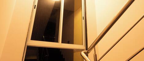 A staircase with a metal handrail and a window with a light fixture above it.