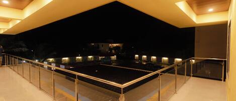 Una terraza amplia al aire libre con baranda de cristal, techo plano y zonas oscuras circundantes.