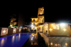 A modern hotel with a swimming pool, multiple balconies, and well-lit exterior. - Shreem Resort (Alibag)