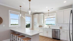 A modern kitchen with white cabinetry, a central island with stools, and a stainless steel refrigerator. - Endless Views | Luxury 4BR Emerald Isle Retreat w/ Pool & Ocean Breezes (Emerald Isle)