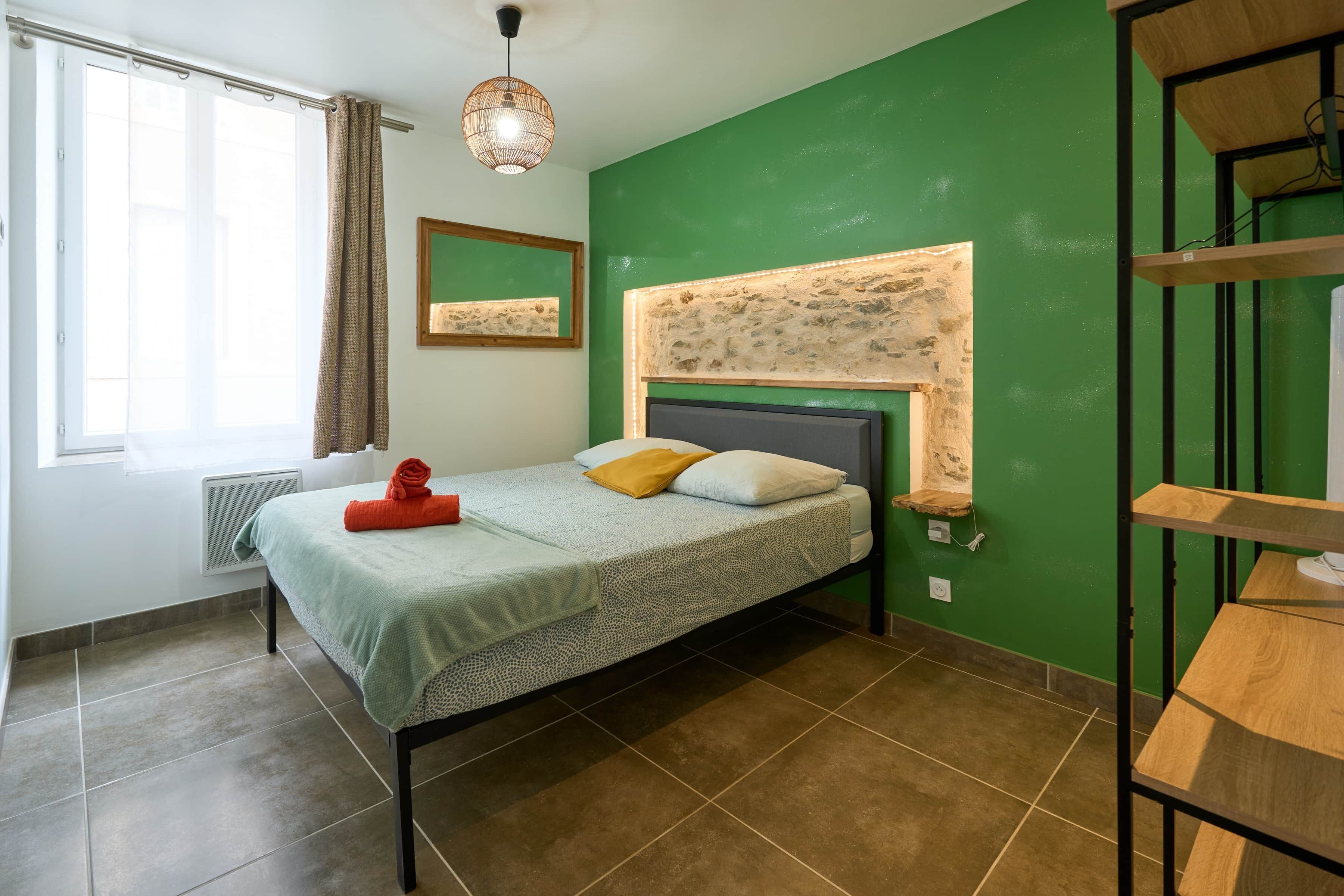 A bedroom with a bed, a window with curtains, a wall-mounted shelf, and a pendant light.