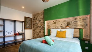 Ein Schlafzimmer mit Bett, grünen Wänden, einer Steinwand, einem Holz-Kopfteil und einer Metallregaleinheit.