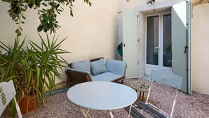 A small patio area with a round table, a sofa with cushions, and a potted plant.