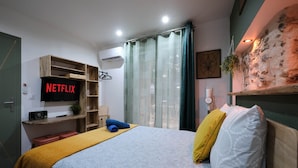 A bedroom with a bed, a TV, a shelf, a window with curtains, and a wall with a textured design.