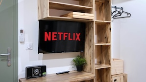 A wooden entertainment unit with a mounted TV displaying the Netflix logo, a remote control, and a small potted plant.