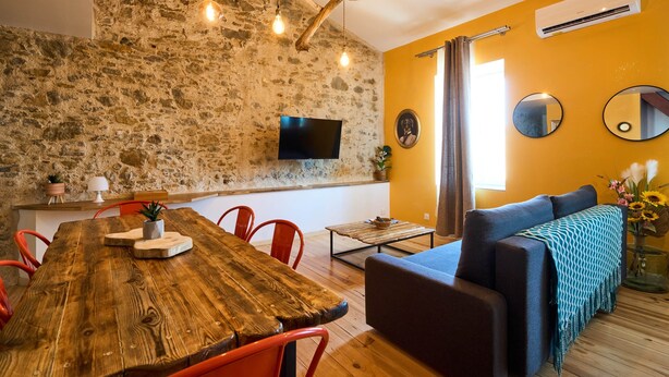 A cozy room with a wooden dining table, red chairs, a blue sofa, and a stone wall. - Unique charm - Clim - 6 pers in the heart of Carca (Carcassonne)