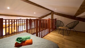 A cozy attic bedroom with a bed, a small table, two chairs, and a wooden railing. - Unique charm - Clim - 6 pers in the heart of Carca (Carcassonne)